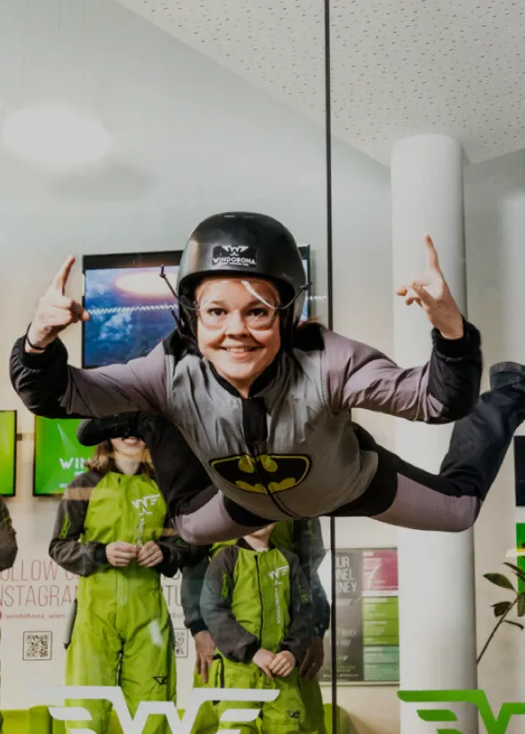 Woman in superhero flight suit flying with thumbs up in tunnel.