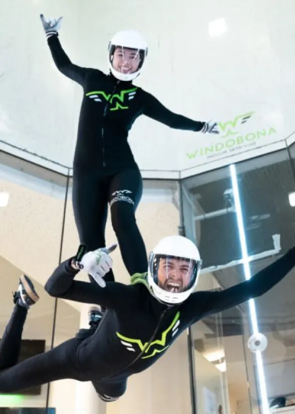 Two people performing tandem indoor skydiving with big smiles.