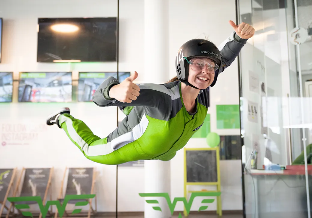 A person smiling and giving thumbs up while flying indoors in a wind tunnel.
