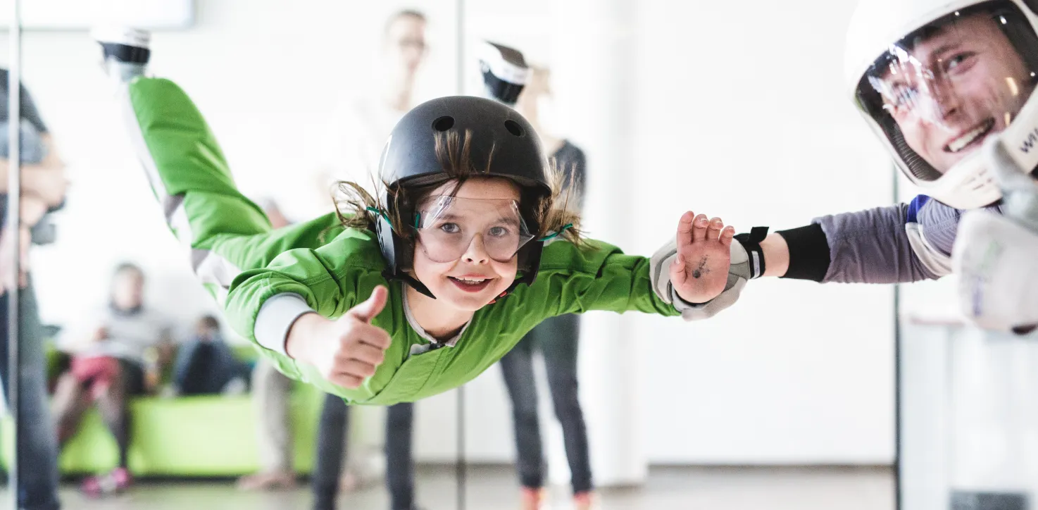 Child flying in wind tunnel, giving a thumbs up to instructor.