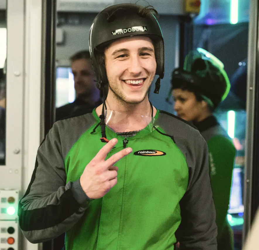 Man in green flight suit smiling and making peace sign