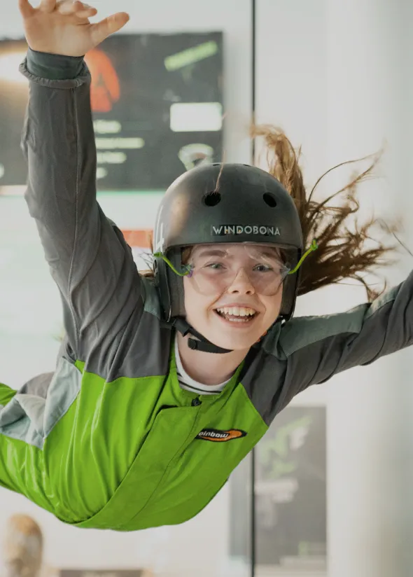 Person skydiving indoors, smiling, in a green jumpsuit.