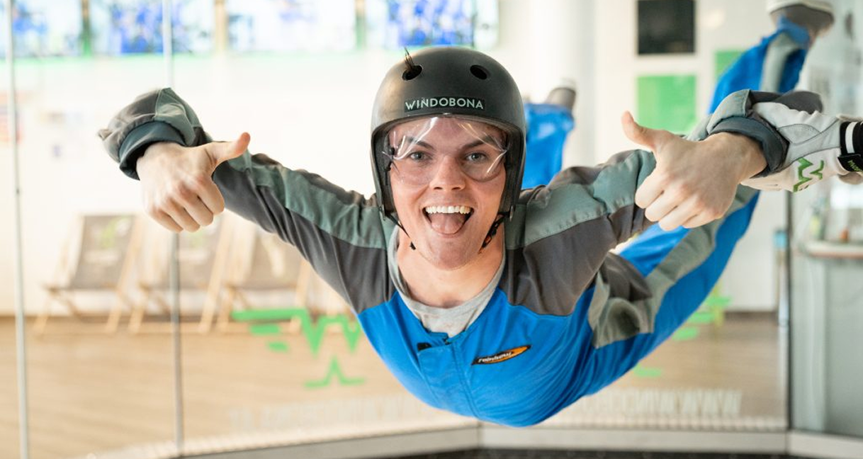 Man skydiving indoors with thumbs up and tongue out