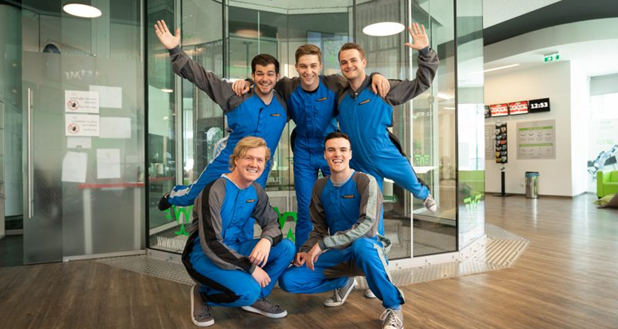 Group of friends in blue flight suits posing at indoor skydiving tunnel