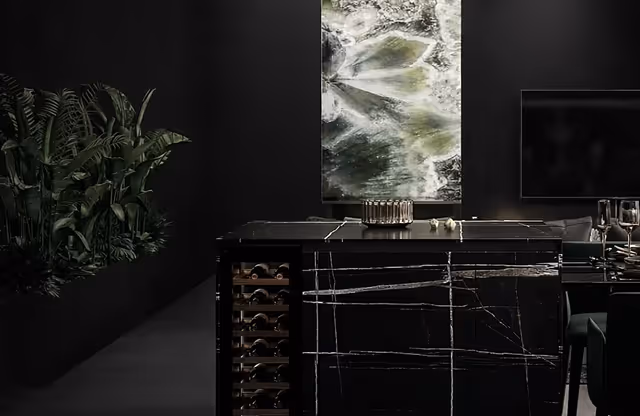 Modern dark kitchen with a black marble kitchen island featuring wine storage, a green plant on the left, abstract artwork on the wall, and a television on the right.