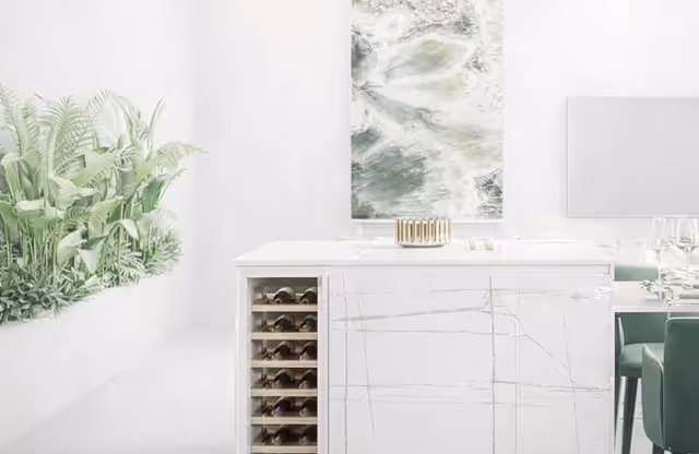 Modern white kitchen island with built-in wine rack, green indoor plants, marble countertop, and abstract wall art.