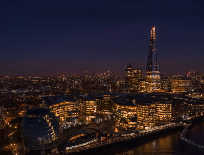 Nighttime cityscape of London featuring illuminated buildings along the River Thames and the Shard skyscraper prominently lit.