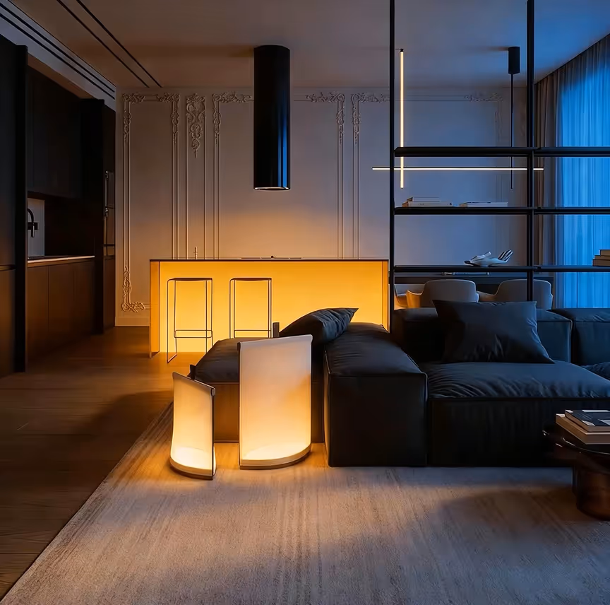 Modern living room with black sofa, glowing floor lamps, illuminated kitchen island, and vertical hanging light fixtures.
