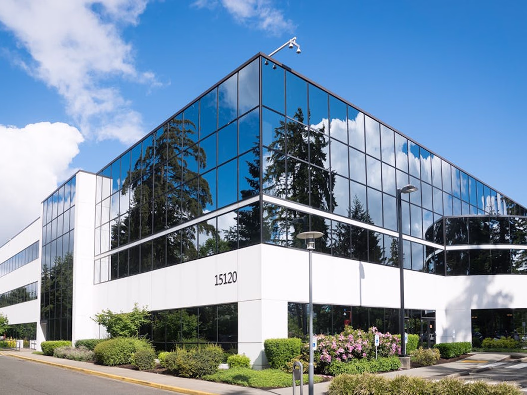 Modern office building with reflective glass windows under a blue sky with clouds.