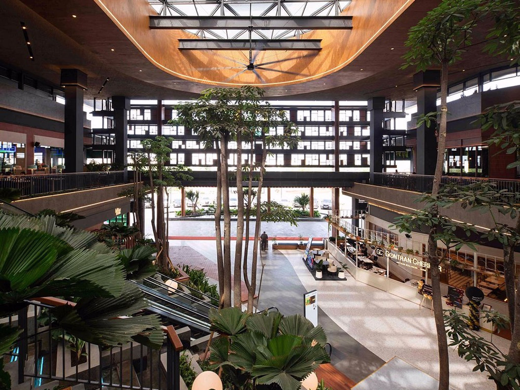Modern shopping mall interior with large skylight, plants, escalators, and shopfronts including Gontran Cherrier.