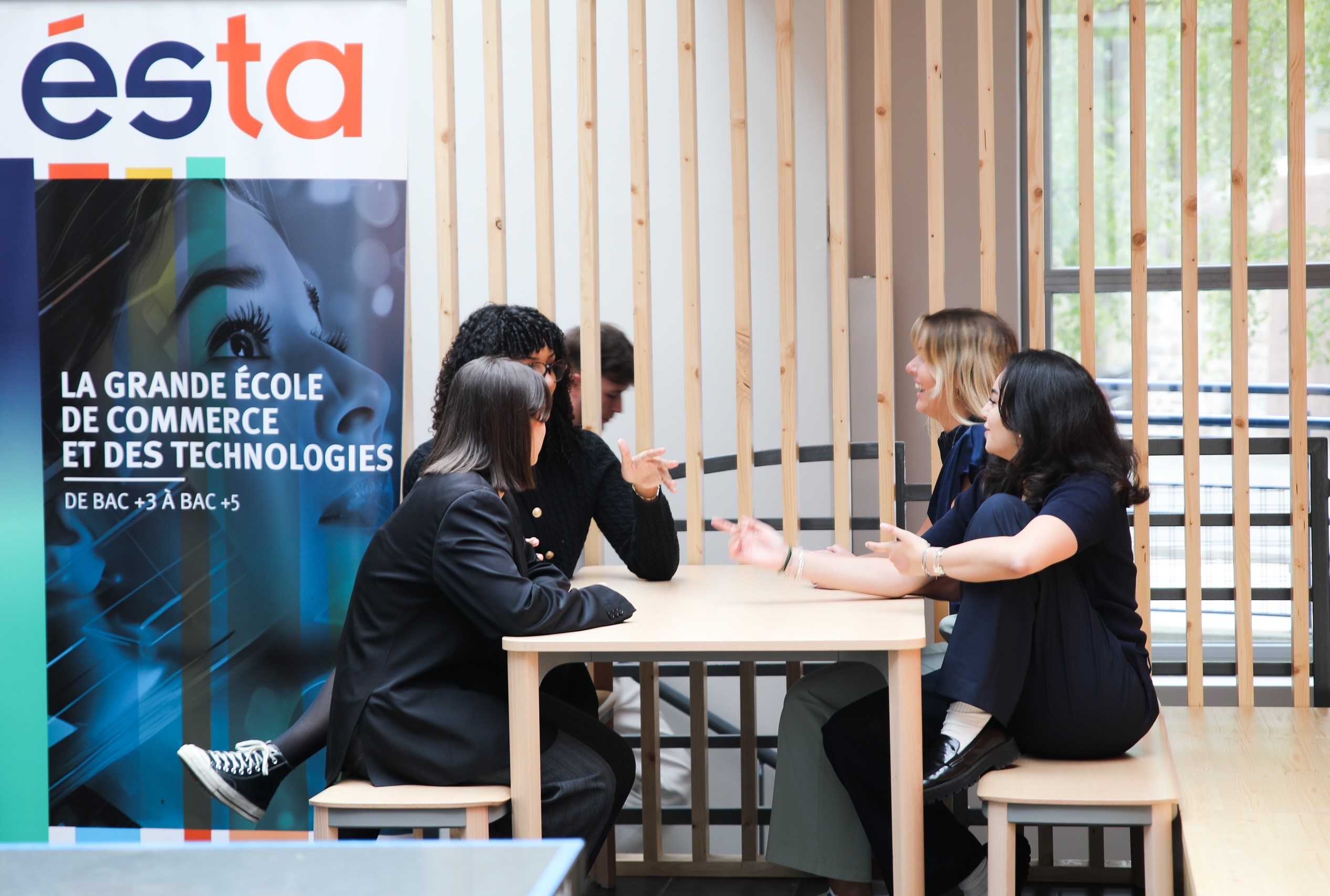 groupe d'étudiants assis à une table en train de discuter avec le panneau de l'école ESTA derrière