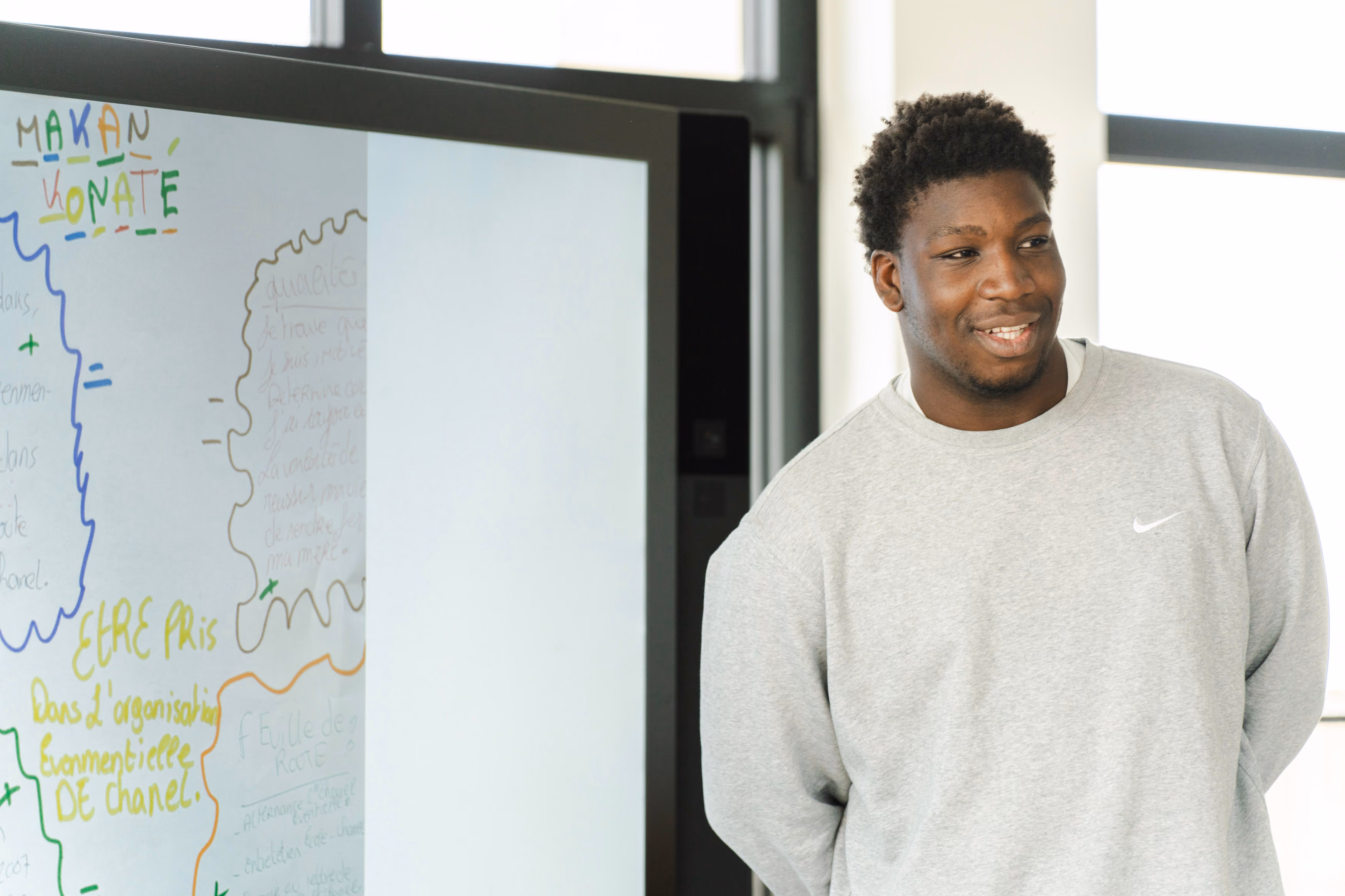 Jeune homme souriant devant un tableau ardoise blanc