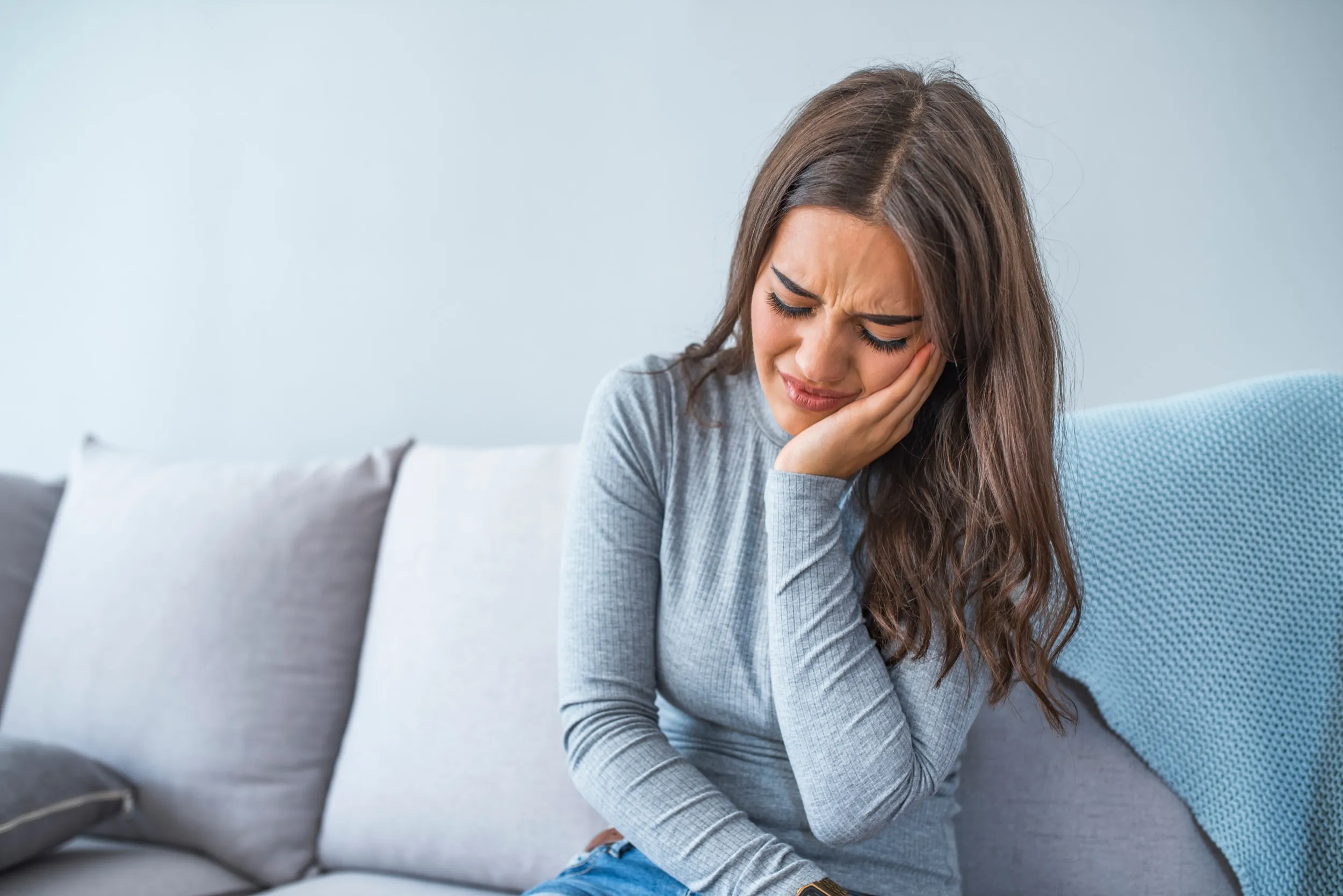 Woman experiencing pain or distress, sitting on couch with hand on face