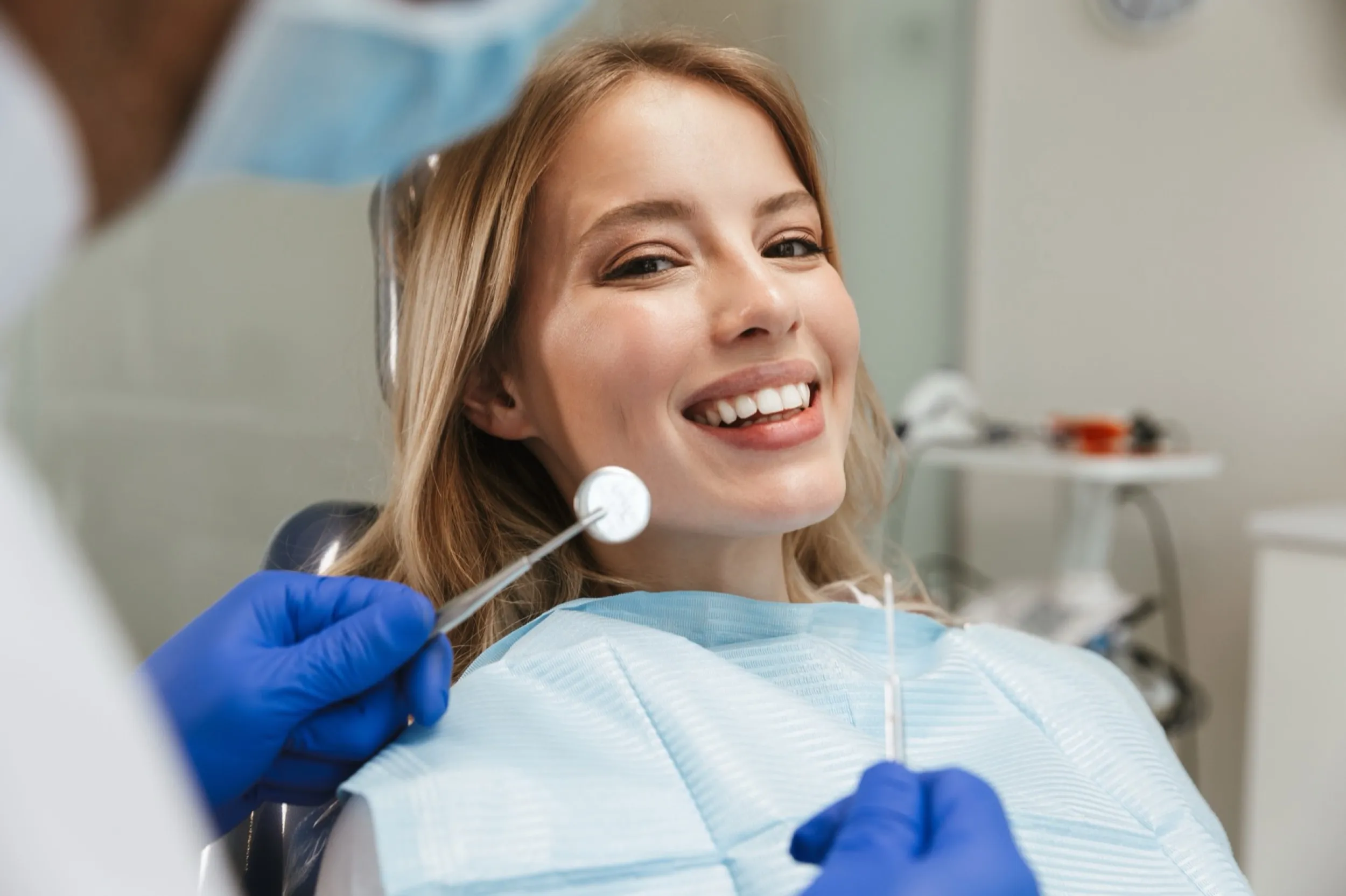 Smiling patient during dental exam with dentist's blue gloved hands