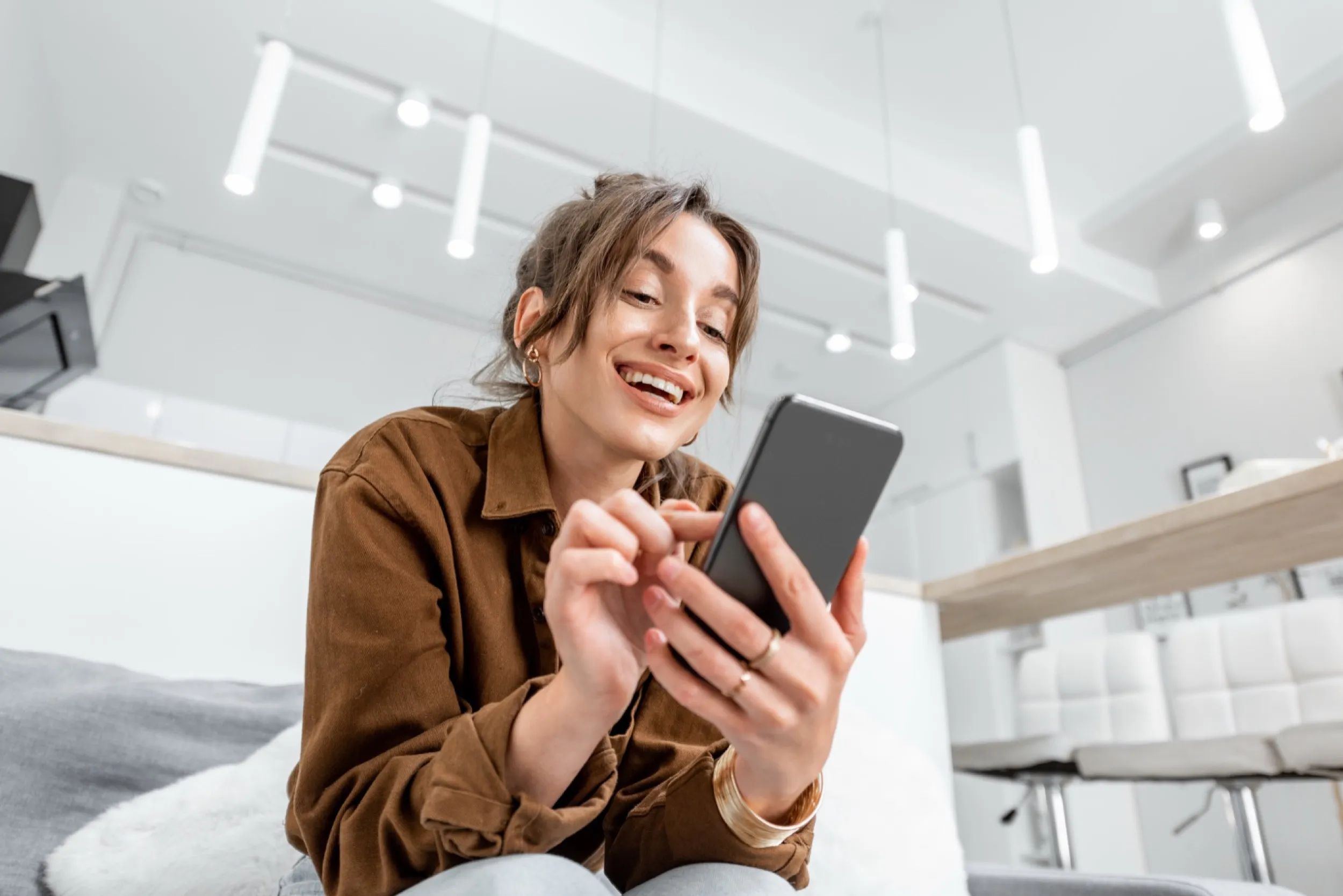 Woman laughing while looking at smartphone in bright modern interior