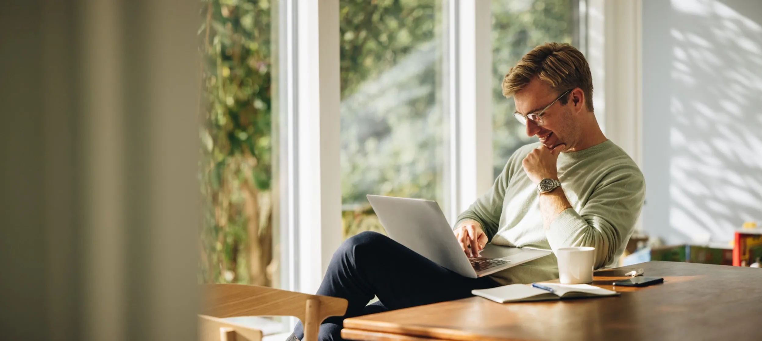 Person working on laptop by window with coffee and books nearby
