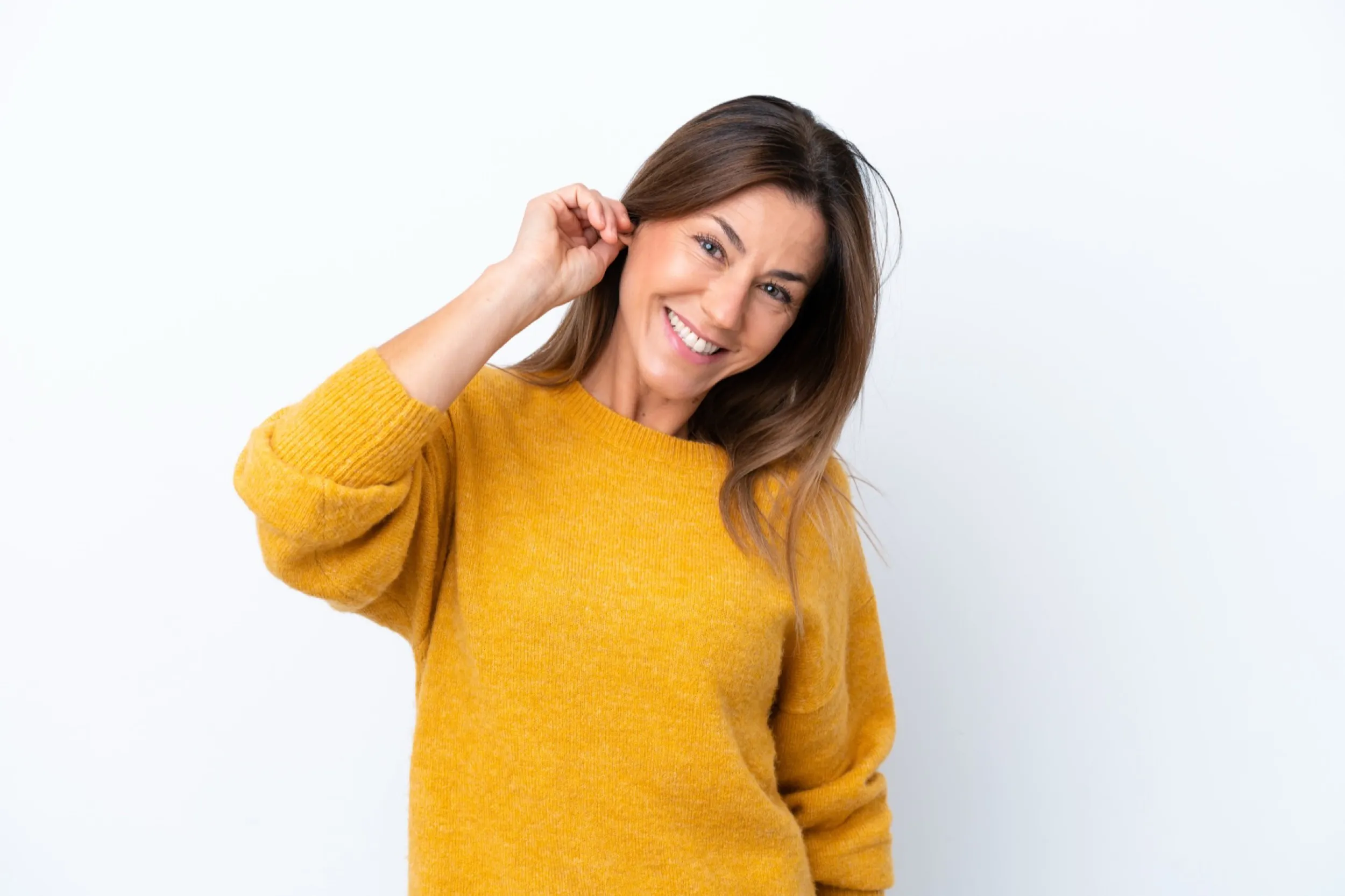Smiling woman in yellow sweater touching hair against white background