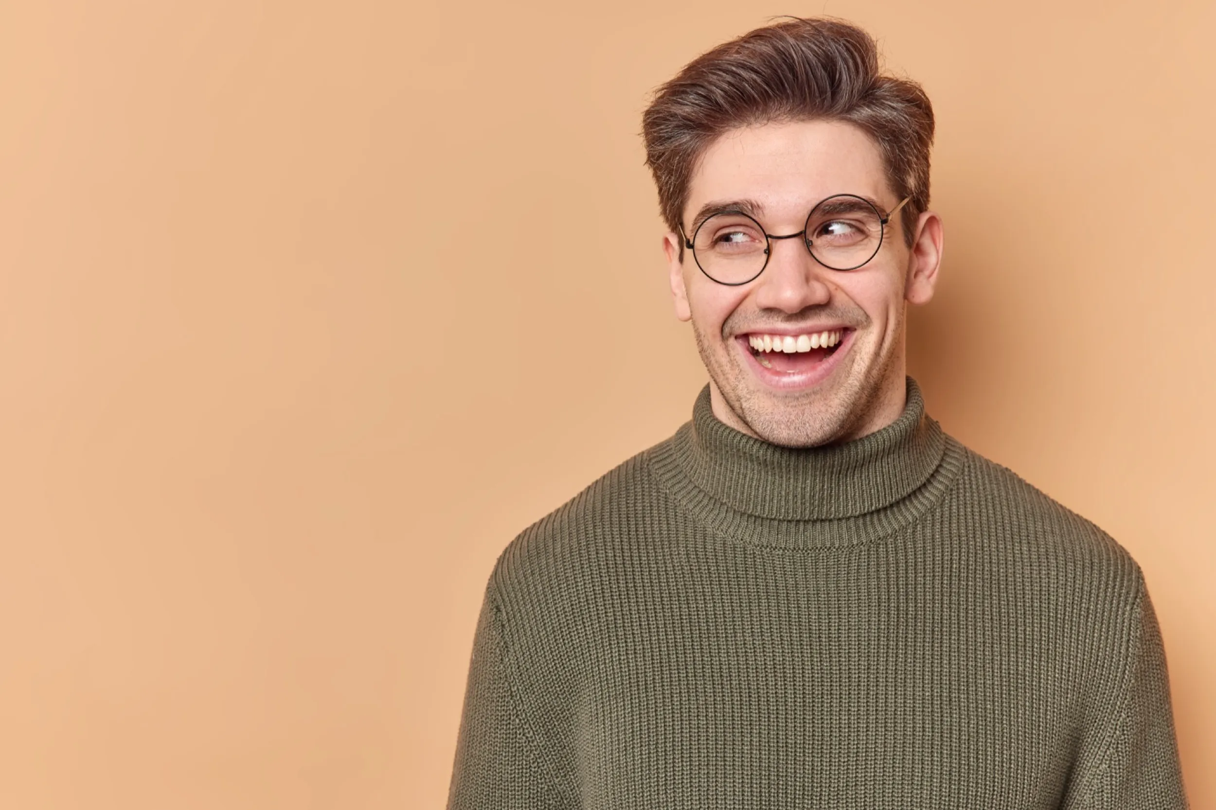 Person in green sweater and glasses laughing joyfully against beige background