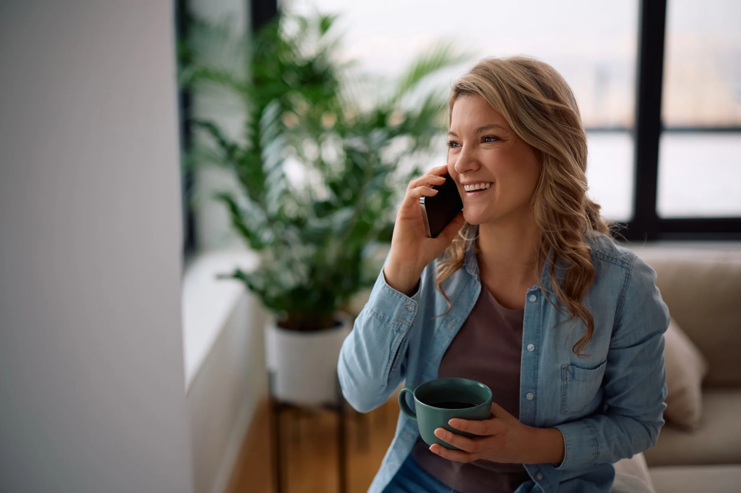 Woman smiling while talking on phone and holding coffee at home