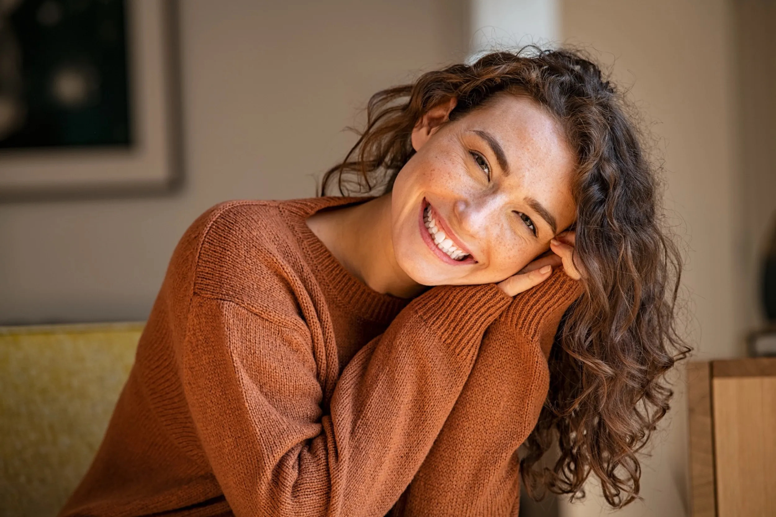 Woman in rust-colored sweater smiling warmly with curly hair