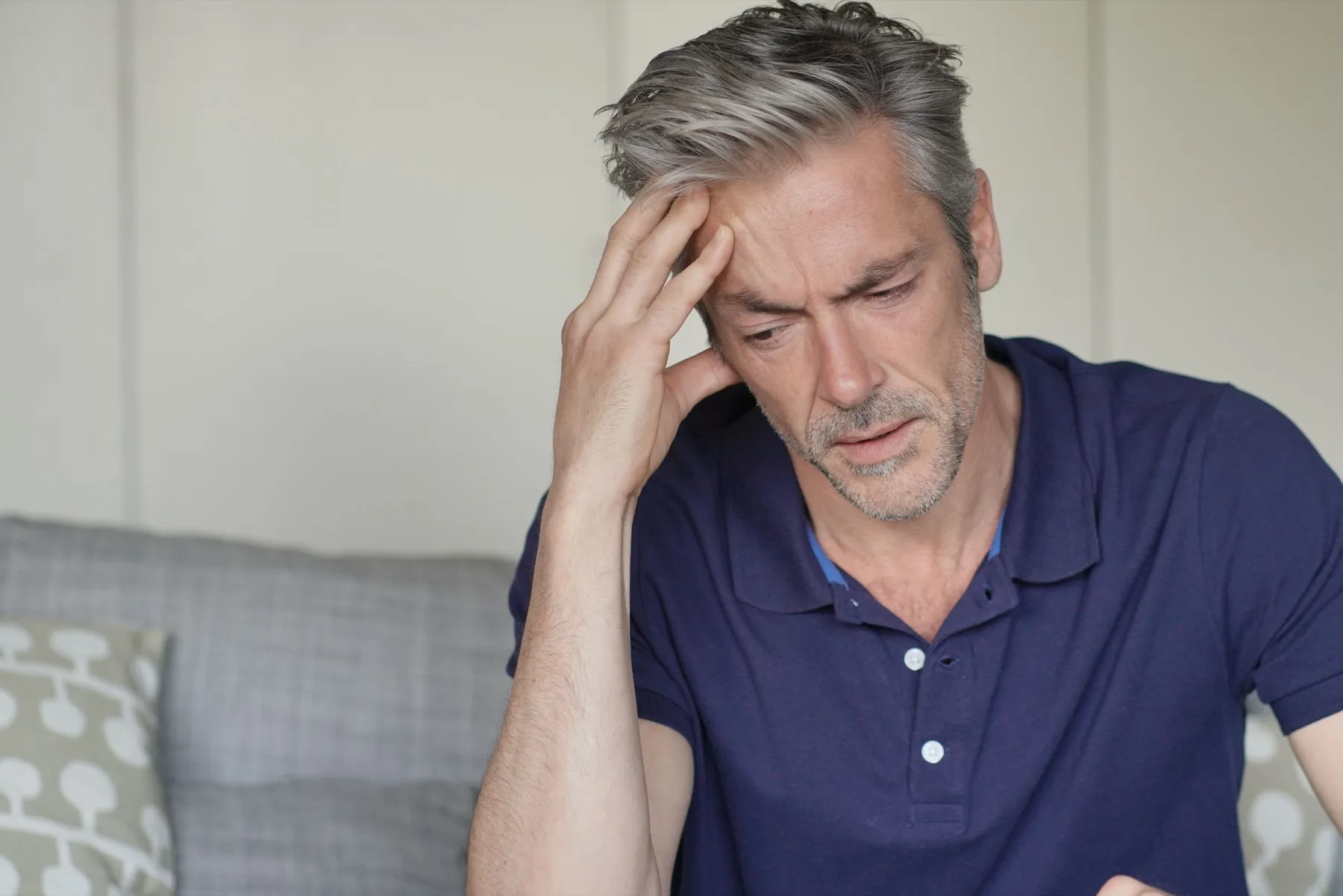 Person with headache holding head, looking stressed and tired on couch