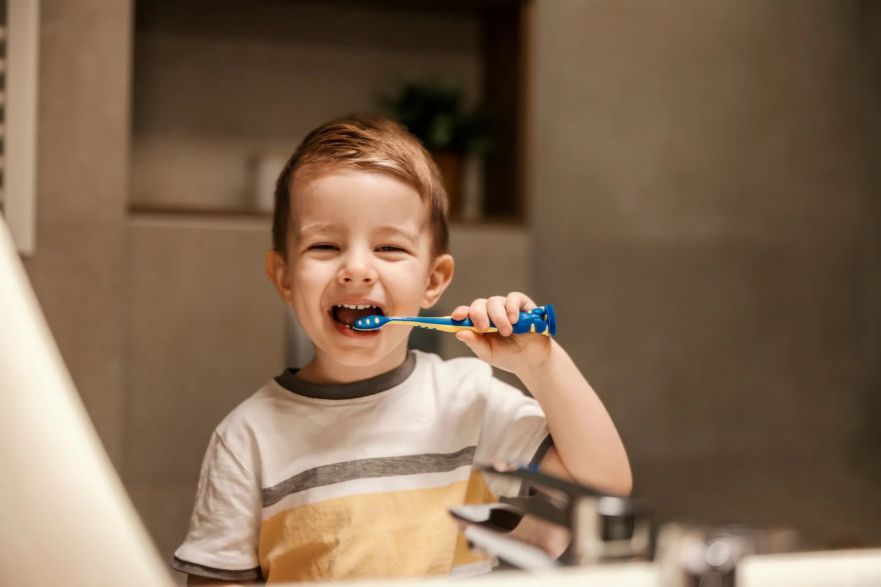 Young child happily brushing teeth with blue toothbrush at home