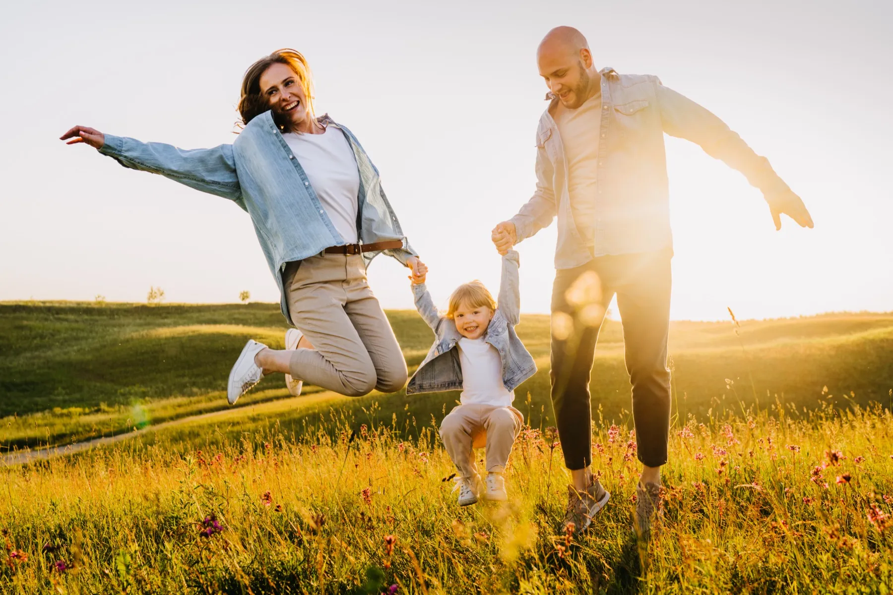 Family jumping together in sunny meadow with wildflowers