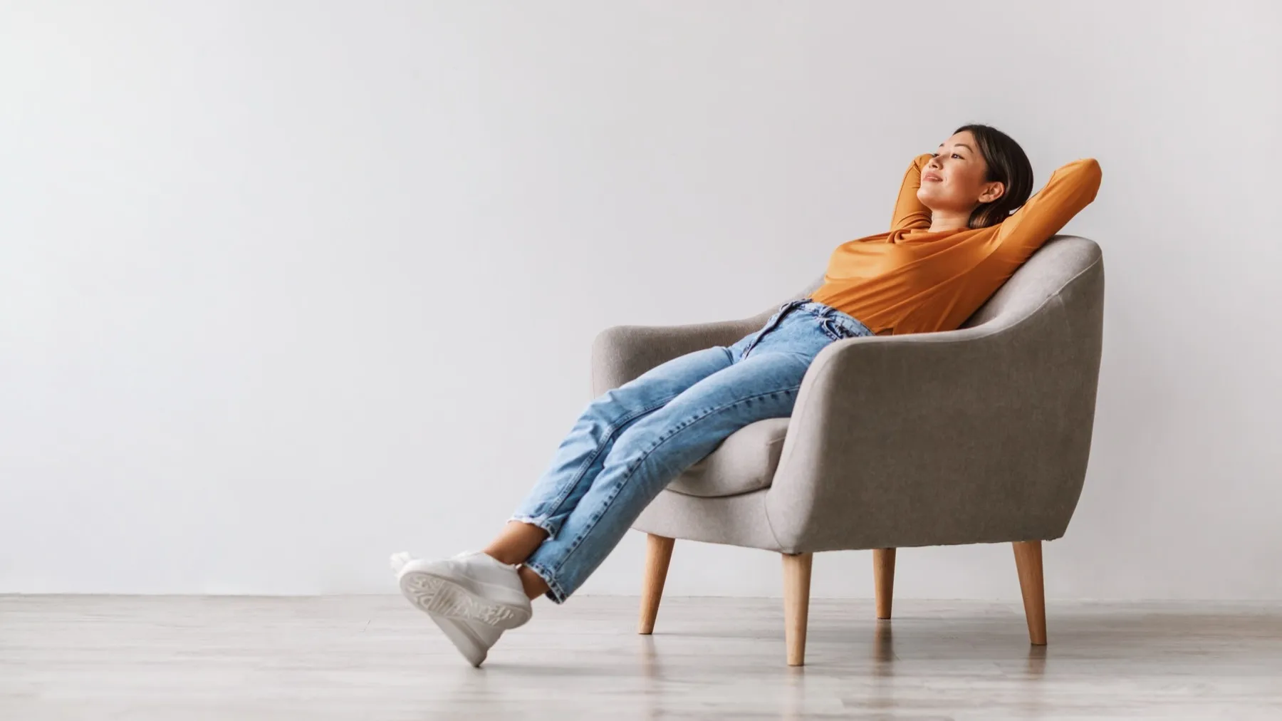 Person relaxing in a gray armchair, wearing orange top and blue jeans