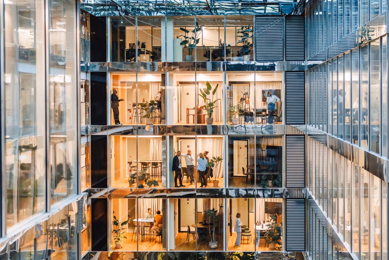 Modern glass office building with multiple floors and people working inside