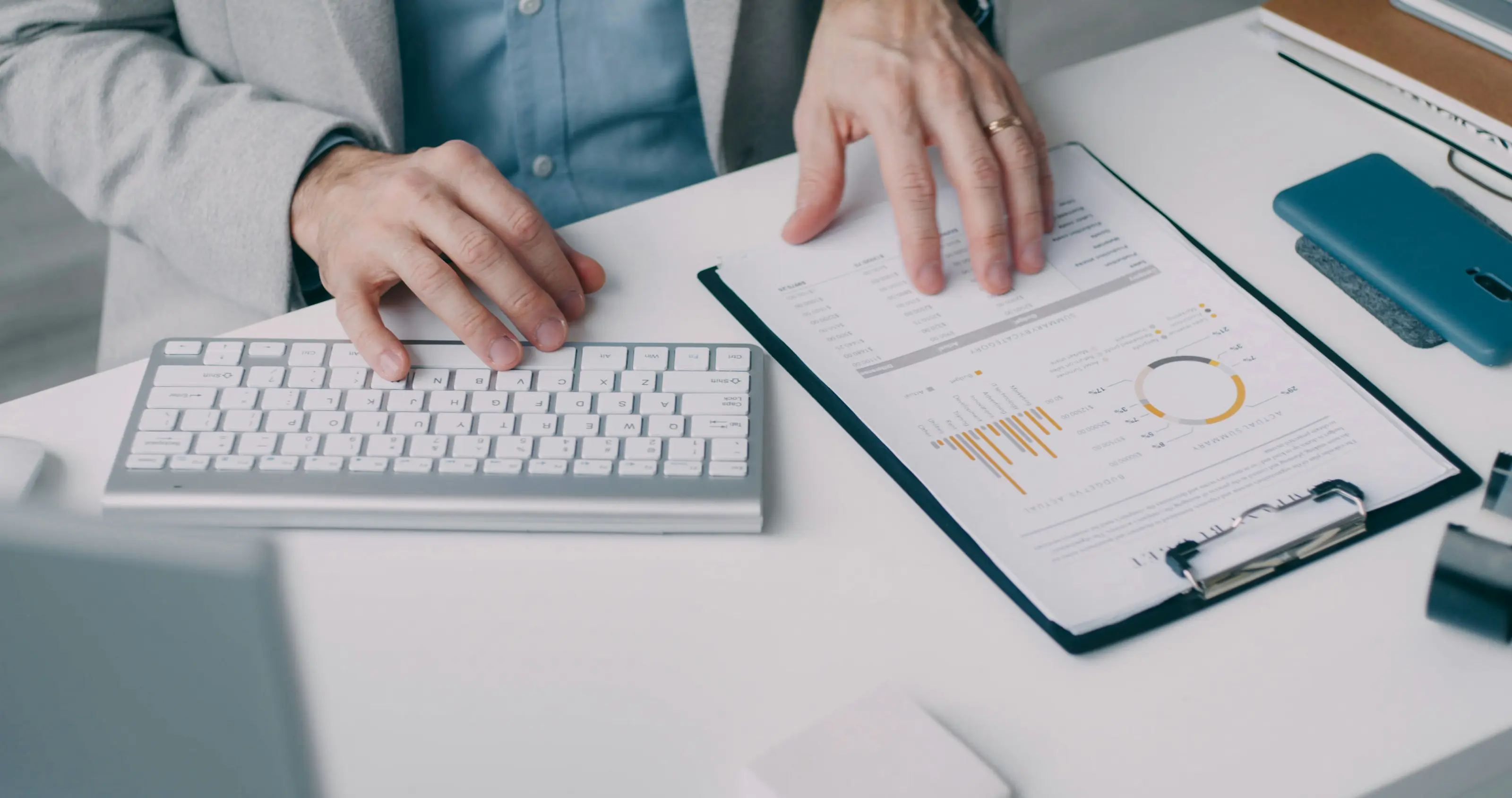 Homme tenant d'une main un document avec des diagrammes et de l'autre côté son clavier d'ordinateur