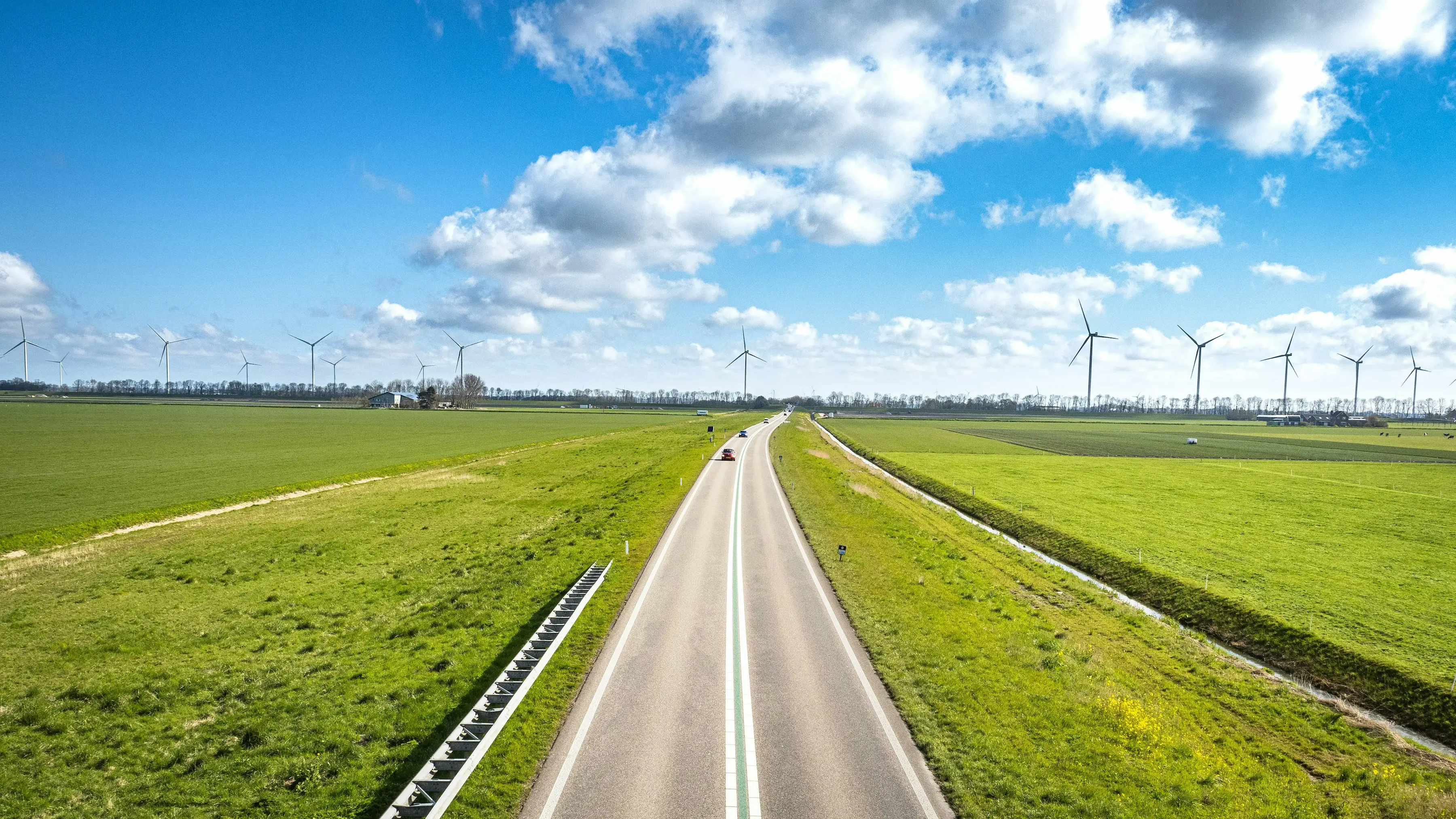 Route au milieu d'un champs verdoyant et des éoliennes au loin