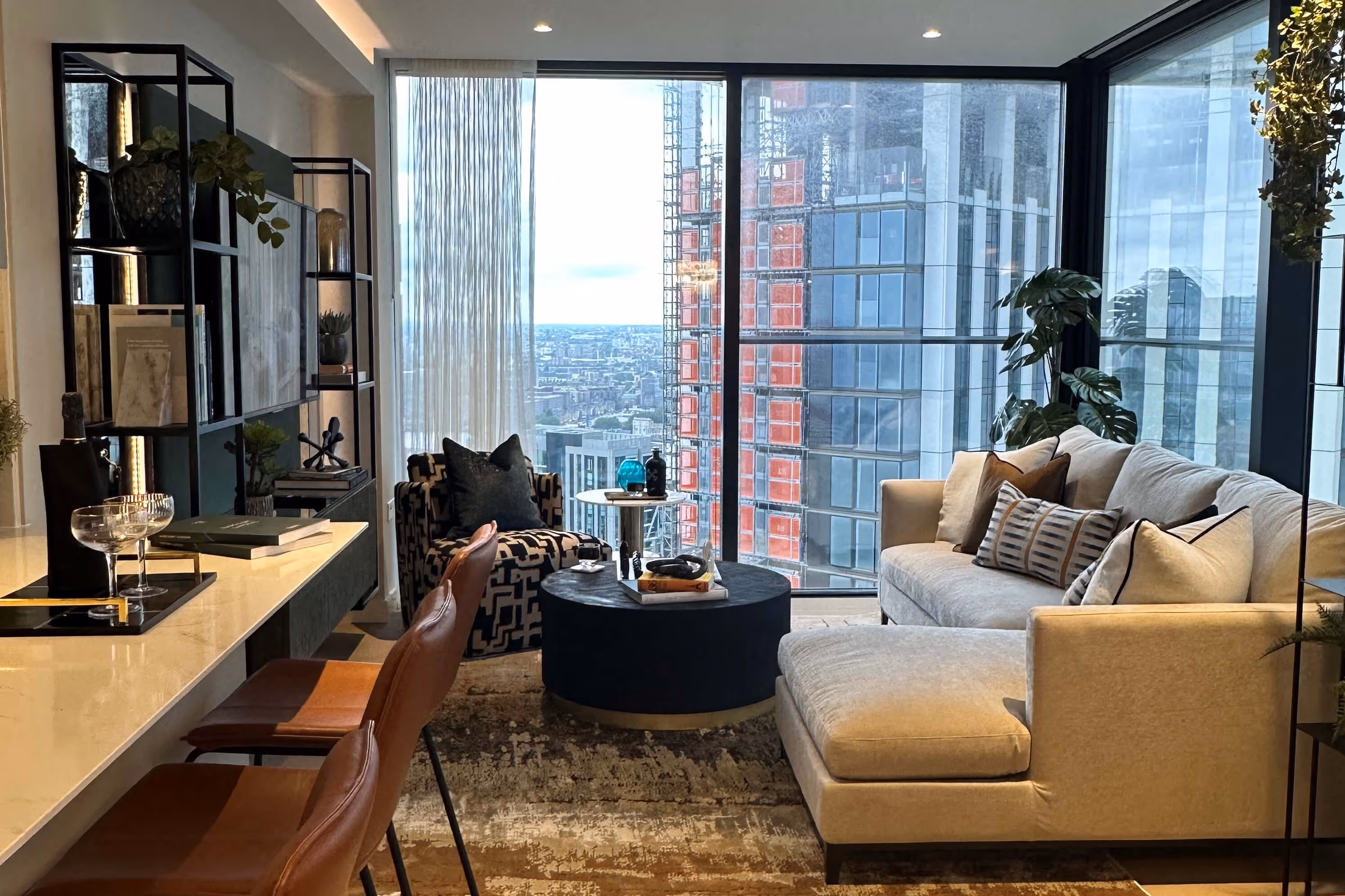 Modern bedroom with white channelled headboard and neutral bedding featuring chevron cushions. A textured mosaic accent wall complements the space, with a black pendant light hanging beside the bed and framed artwork on the white wall.