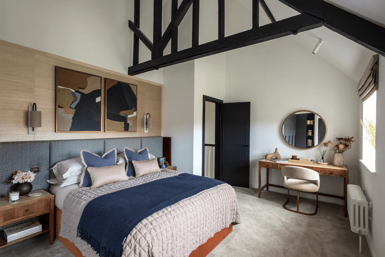 Primary bedroom at Trent Park, The Buckingham Royal Mews, with a vaulted beamed ceiling, navy and beige bedding, and a pair of abstract prints above the headboard.