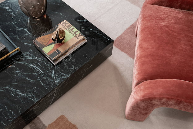 Close-up of a green marble coffee table with a smoked glass vase and stacked design books beside the terracotta velvet armchair.