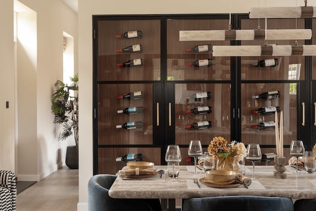 Dining area set for entertaining with navy velvet chairs, a sculptural pendant light, and a built-in glass-fronted wine cabinet.