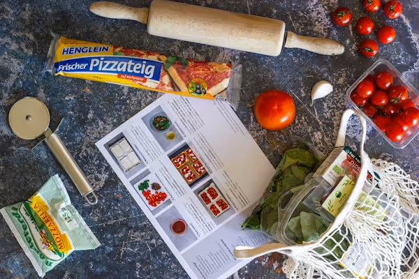 A cookbook surrounded by pizza ingredients and a rolling pin.