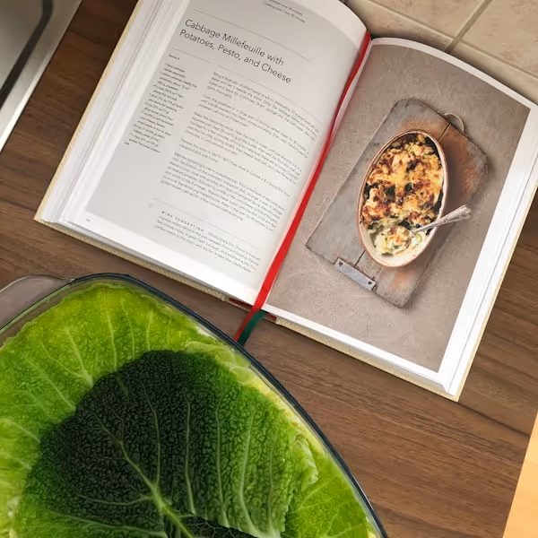A cookbook with greens beside it.