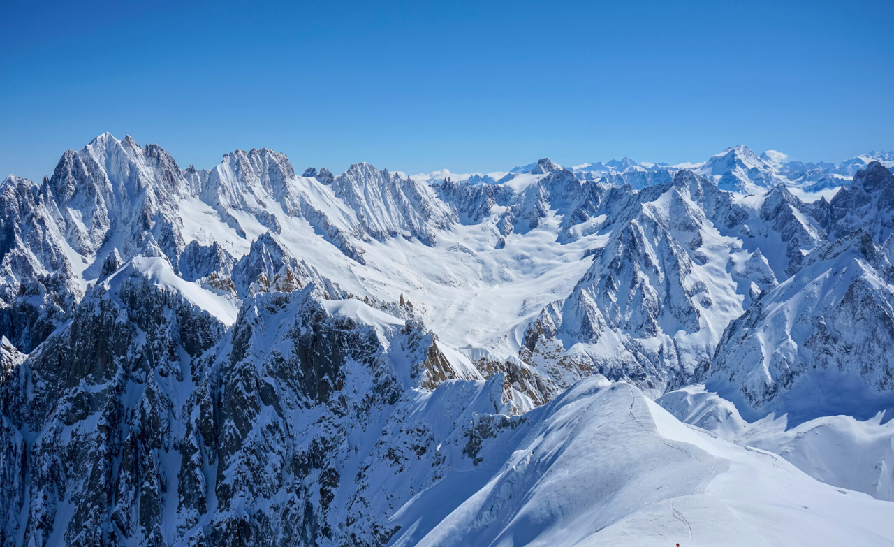 Vue panoramique sur les sommets enneigés du massif du Mont-Blanc sous un ciel bleu.