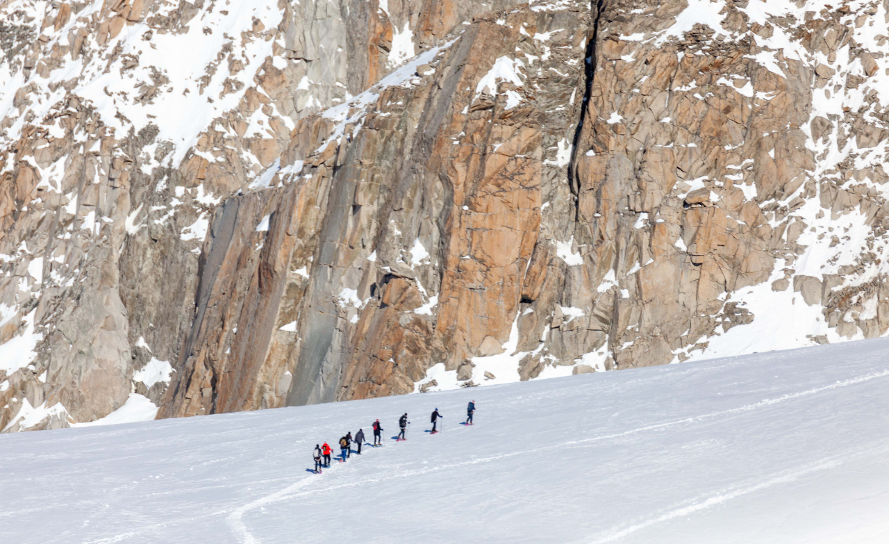 Cordée d’alpinistes avançant sur un glacier enneigé au pied d’une paroi rocheuse dans le massif alpin.