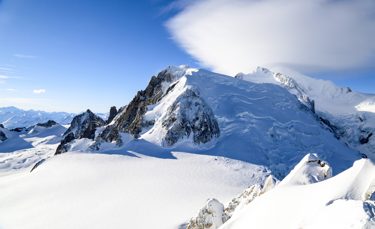 Vue sur un sommet enneigé et ses glaciers dans le massif du Mont-Blanc sous un ciel bleu.