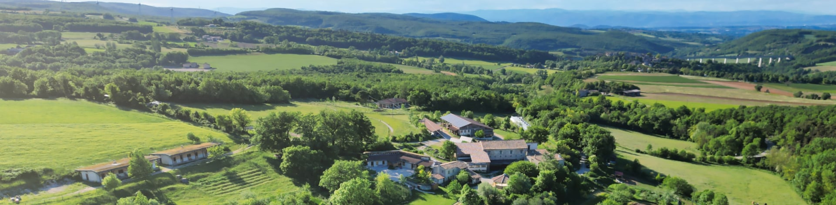 Vue aérienne d’un domaine entouré de forêts et de champs verdoyants dans un paysage vallonné.