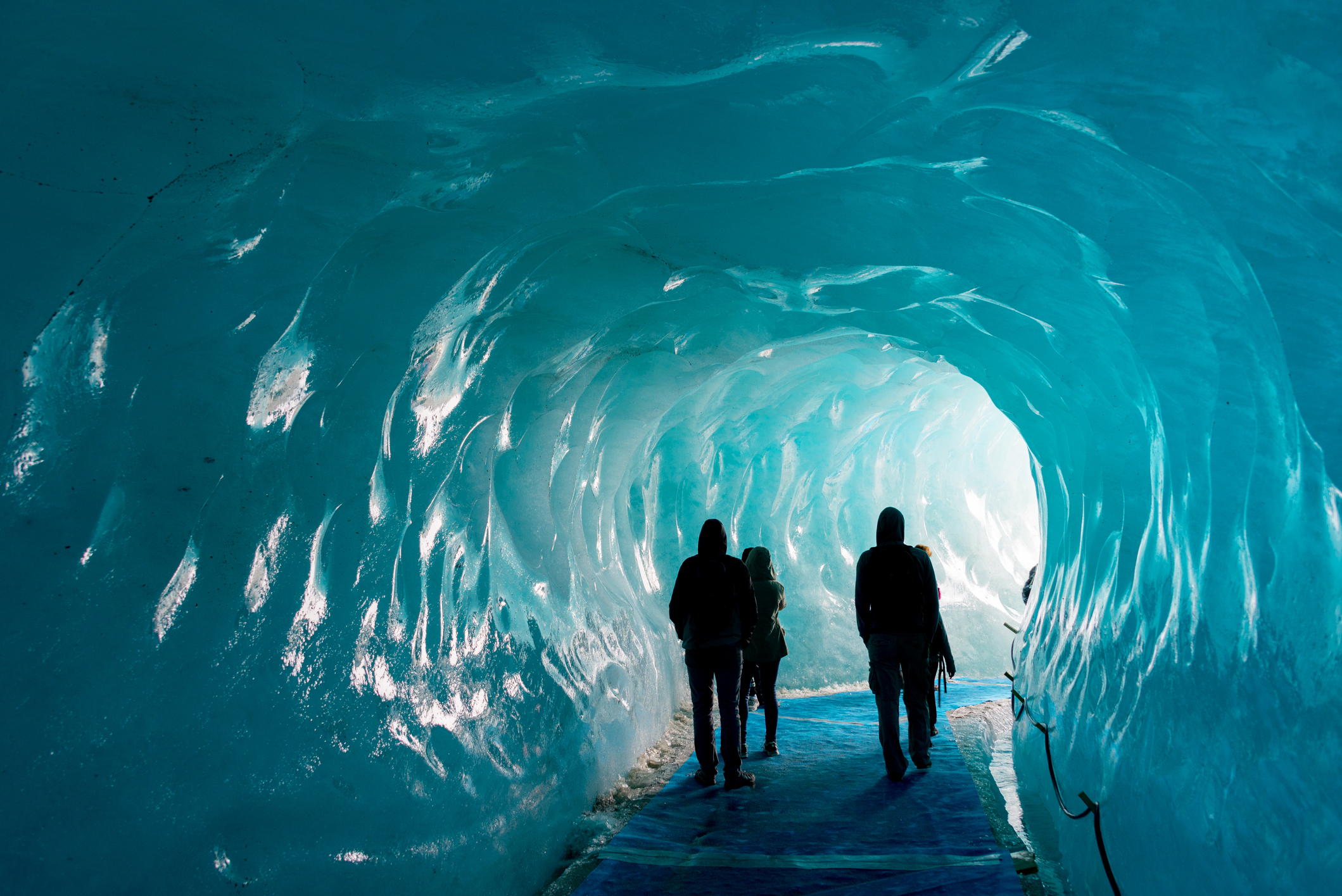 Groupe de personnes marchant à l’intérieur d’une grotte de glace aux parois bleutées.