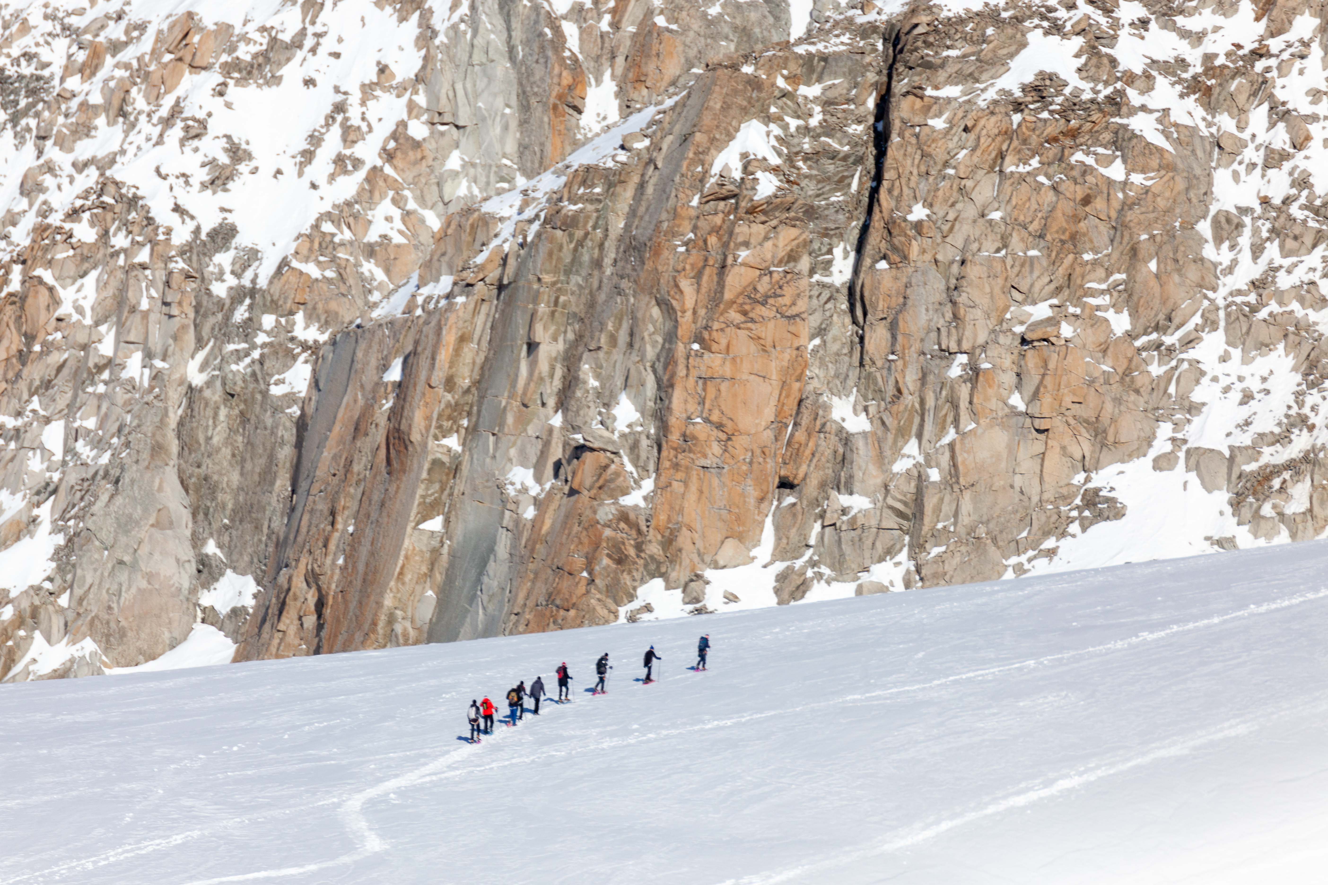 Groupe d'alpinistes progressant en cordée sur un glacier enneigé, au pied d'une paroi rocheuse dans le massif du Mont-Blanc.