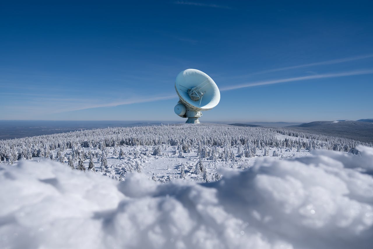 Grande antenne parabolique installée au sommet d’une forêt enneigée, sous un ciel bleu dégagé.