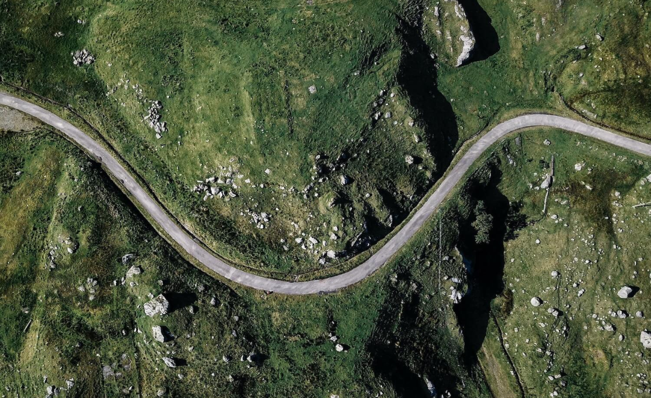 Vue aérienne d’une route sinueuse traversant un paysage vert et rocheux en montagne.