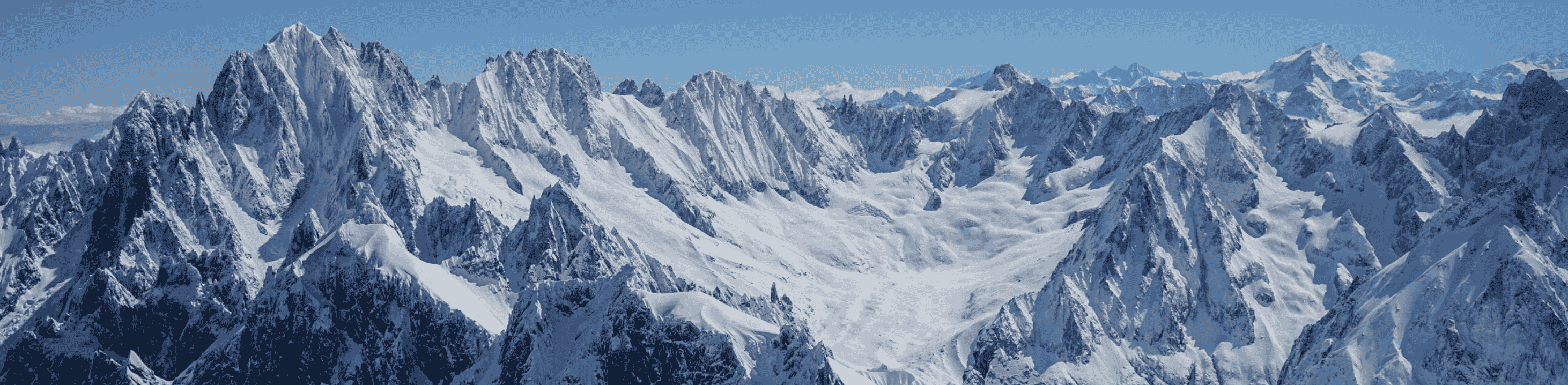 Panorama sur les sommets enneigés des Alpes avec de vastes glaciers et un ciel dégagé.