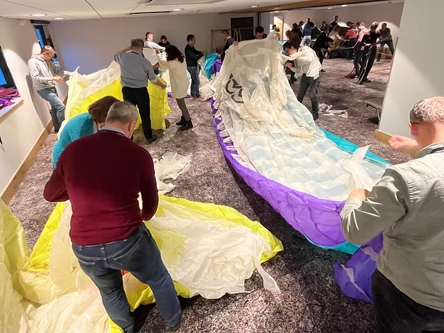 Participants à un séminaire d’entreprise lors d’un atelier de team building en intérieur, dépliant collectivement des voiles de parapente.