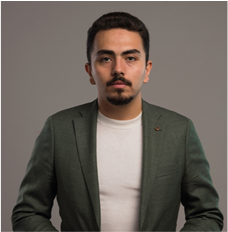 Man with short dark hair and mustache wearing a green blazer and white shirt against a gray background.