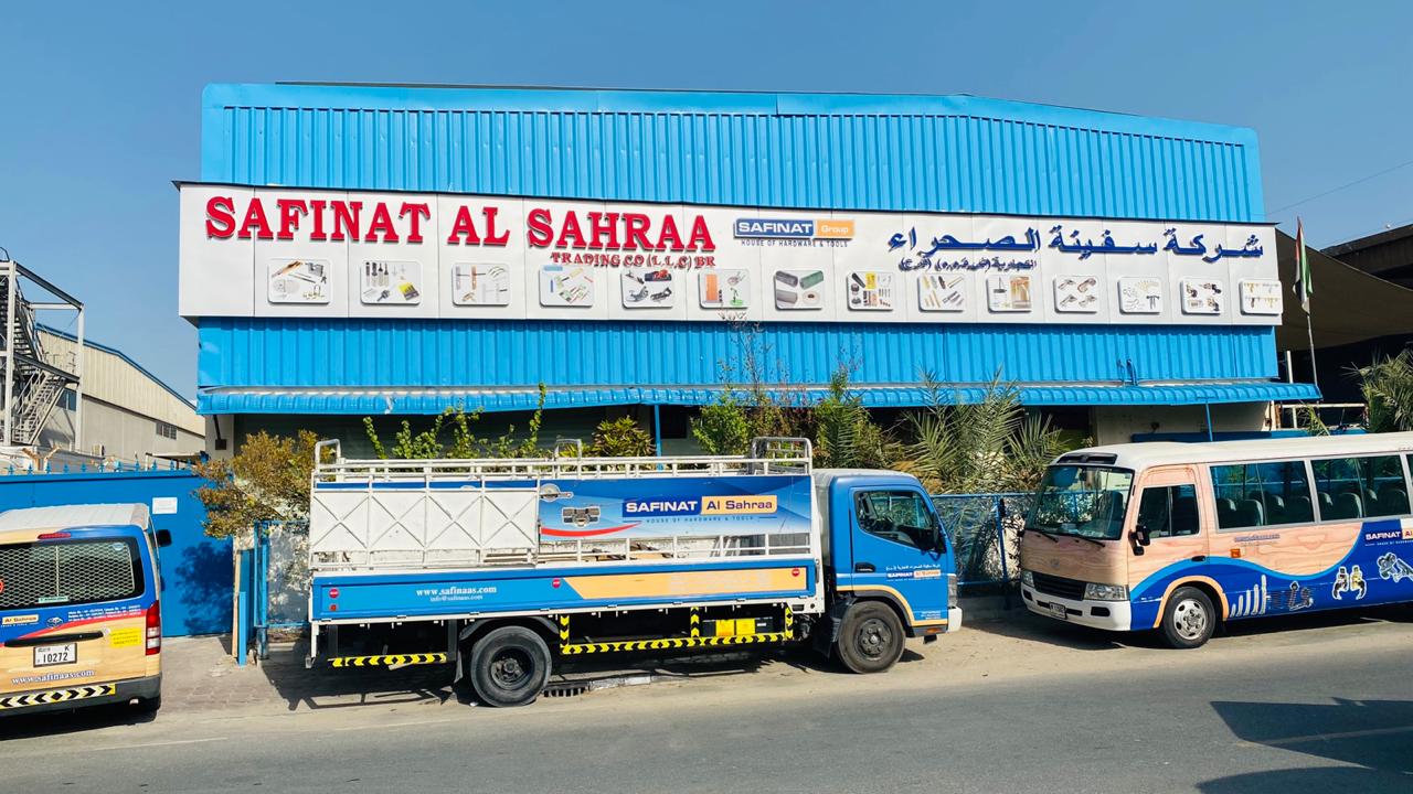 Blue and white building with a large sign reading 'SAFINAT AL SAHRAA' above three parked vehicles branded with the same company name.