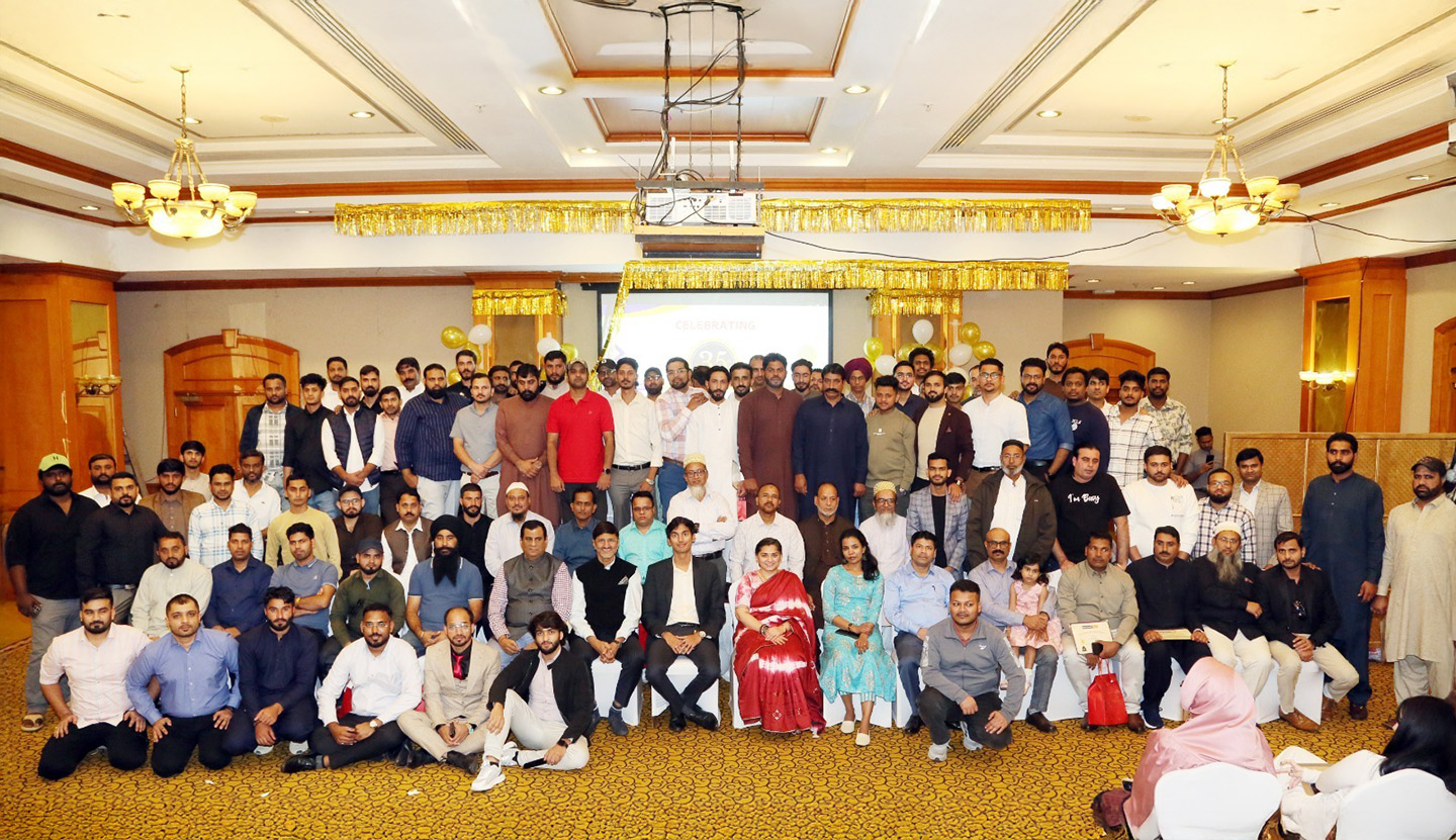 Large group of men and women posing for a formal group photo in a banquet hall decorated with gold balloons and streamers.
